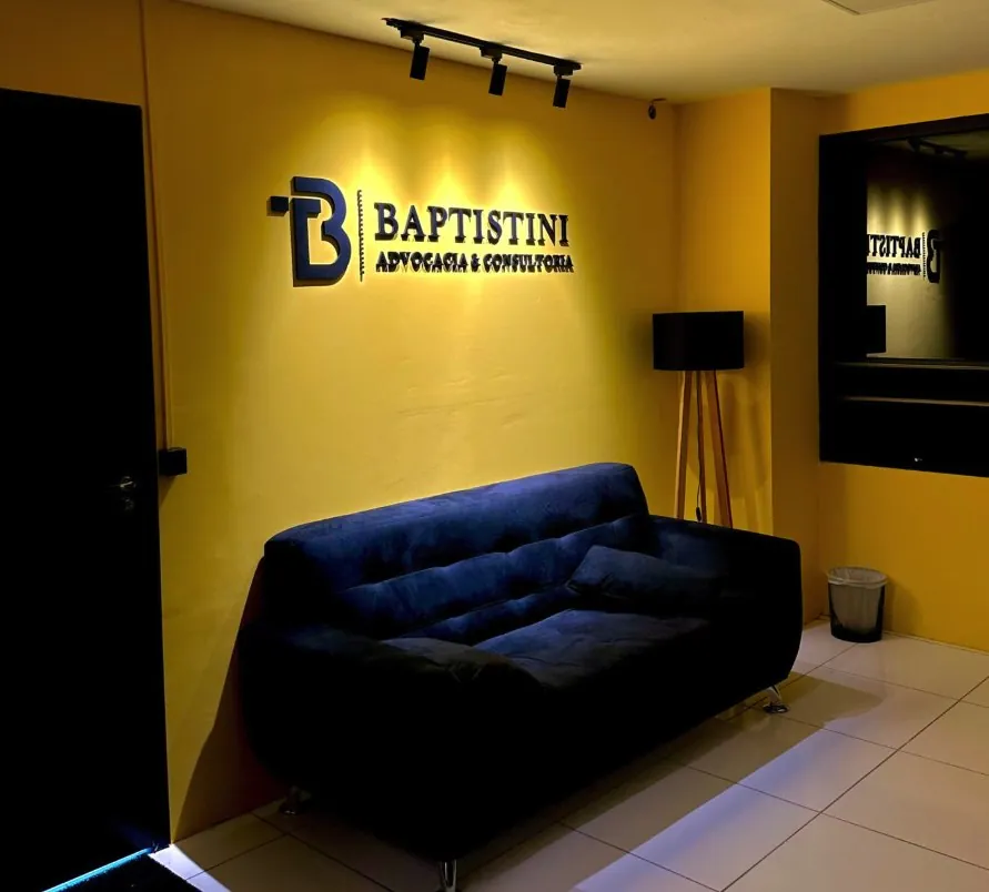 Recepção do escritório com a marca Baptistini iluminada na parede amarela